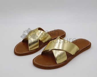 May include: Two pairs of gold leather sandals with brown leather soles. The sandals have a criss-cross strap design.
