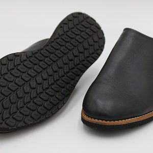 Könnte beinhalten: Ein Paar schwarze Lederschlappen mit Gummisohle. Die Schlappen haben ein schlichtes Design und sind perfekt zum Entspannen zu Hause.