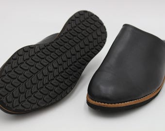 May include: A pair of black leather slippers with a rubber sole. The slippers have a simple design and are perfect for lounging around the house.
