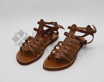 May include: A pair of brown leather gladiator sandals with multiple straps and buckles. The sandals have a woven design and a flat sole.