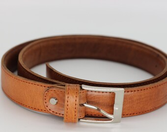 May include: A coiled, light brown leather belt with a silver-colored buckle. The belt has a classic design with visible stitching along the edges. The buckle is rectangular and has a single prong.