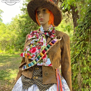 May include: A brown and gold brocade jacket with a colorful butterfly print scarf and a spool of thread accessory. The jacket has a high collar and a fitted silhouette. The model is wearing a tall brown top hat with a red band and a white and gray skirt with a floral print.