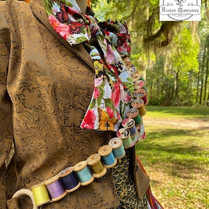 May include: A brown jacket with a floral print scarf and a string of colorful spools of thread. The jacket has a gold pattern and the spools are attached to a brown leather belt. The image includes the text "Kraken Costumes".