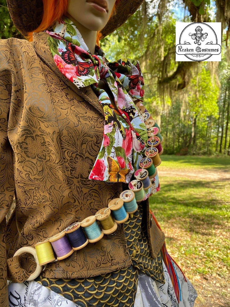 May include: A brown jacket with a floral print scarf and a string of colorful spools of thread. The jacket has a gold pattern and the spools are attached to a brown leather belt. The image includes the text "Kraken Costumes".