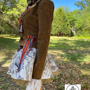 May include: A brown jacket with a floral pattern and a white and black skirt with a print of text and images. The jacket has a colorful tassel hanging from the side. The skirt has a white lace trim.