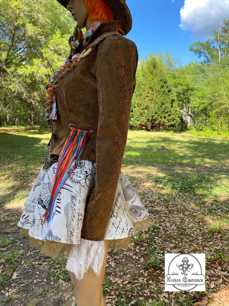 May include: A brown jacket with a floral pattern and a white and black skirt with a print of text and images. The jacket has a colorful tassel hanging from the side. The skirt has a white lace trim.