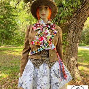 May include: A brown and gold Mad Hatter costume with a tall brown top hat, a brown jacket with a gold vest, a white and black patterned skirt, and a colorful bow tie. The costume is worn by a mannequin with orange hair.