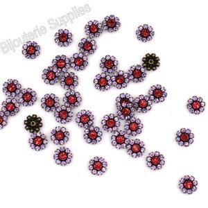 May include: A scattering of small, red and purple flower-shaped embellishments with rhinestones. The embellishments have a bronze-colored metal backing.