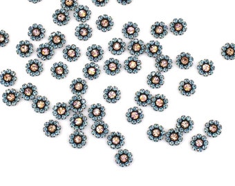 May include: A scattering of light blue and iridescent flower-shaped rhinestones on a white background.  The rhinestones are about 1/2 inch in diameter.