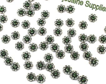 May include: A scattering of green and silver flower-shaped embellishments on a white background.  The embellishments are about 1 cm in diameter.  The text "Bijouterie Supplies" is visible in the upper right corner of the image.