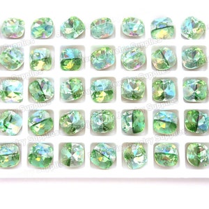 May include: A tray of 36 square-shaped green iridescent glass rhinestones. The rhinestones are arranged in a grid pattern and are all the same size.