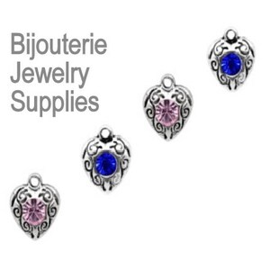 May include: Four silver heart-shaped charms with different colored rhinestones. The charms are for jewelry making and crafting.