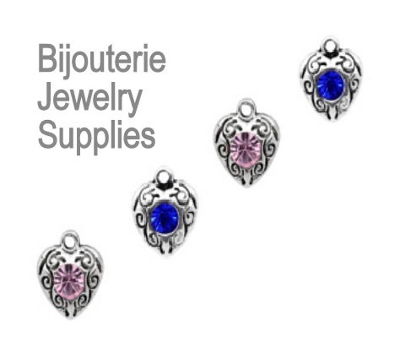 May include: Four silver heart-shaped charms with different colored rhinestones. The charms are for jewelry making and crafting.