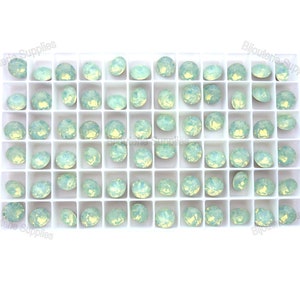 May include: A white plastic tray filled with 49 light green opal rhinestones. The rhinestones are arranged in a grid pattern.