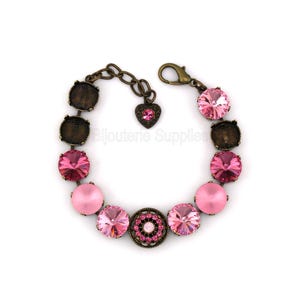 May include: A pink and bronze bracelet with a variety of round and oval-shaped pink crystals and beads. The bracelet has a heart-shaped charm and a clasp closure. The metal has a bronze finish.