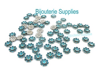 May include: A large quantity of silver and turquoise blue flower-shaped embellishments. The embellishments are scattered on a white background. The text "Bijouterie Supplies" appears at the top of the image.