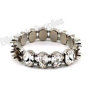 May include: A silver bracelet with clear oval-shaped rhinestones. The bracelet is made of metal and has a stretchy design.