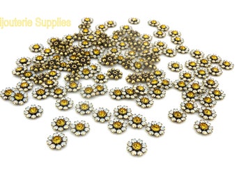 May include: A large quantity of small, gold-toned flower-shaped embellishments with clear rhinestones. Each flower has a yellow center.
