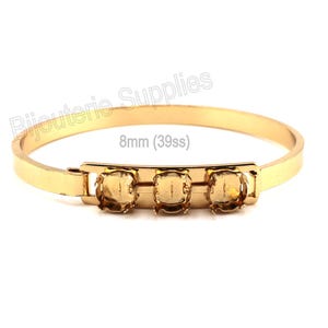 May include: A gold-toned metal bangle bracelet featuring three empty prong settings for 8mm (39ss) stones. The bracelet has a smooth, polished finish and a hinged clasp mechanism. The text "Bijouterie Supplies" and "8mm (39ss)" is visible.