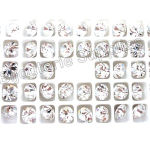 May include: A white plastic tray filled with 48 clear round rhinestones. The rhinestones are arranged in a grid pattern.