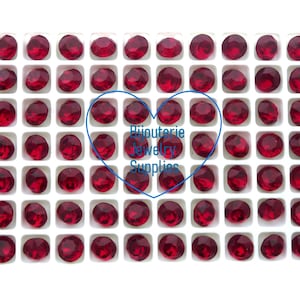 May include: A close-up view of a white tray filled with 100 small, round, red rhinestones. The rhinestones are arranged in a grid pattern. The text "Bijouterie Jewelry Supplies" is visible in the center of the image.