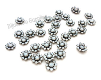 May include: A collection of flower-shaped embellishments with a central white opal-like stone surrounded by smaller clear stones. The metal setting has an antique silver finish. The embellishments are scattered on a white surface.