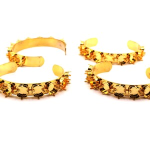 May include: Four gold-toned metal cuff bracelets, each featuring a series of empty circular prong settings along the outer edge. These open-ended bangles are designed for holding stones or cabochons and have a polished, reflective finish.