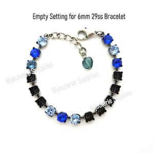 May include: Empty setting for a 6mm 29ss bracelet with a silver chain and a heart-shaped charm. The setting is designed to hold round stones and features a variety of blue and light blue stones.