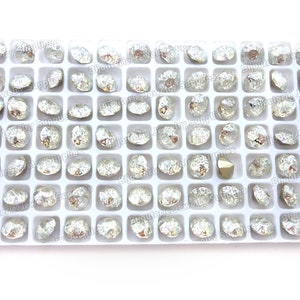 May include: A white plastic tray filled with 49 clear, faceted, round, glass rhinestones. The rhinestones have a silver, iridescent finish.