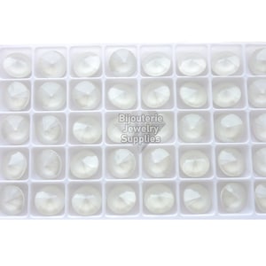 May include: A white plastic tray filled with 36 clear, round, faceted glass rhinestones. The rhinestones are arranged in a grid pattern. The tray is labelled "Bijouterie Jewelry Supplies".