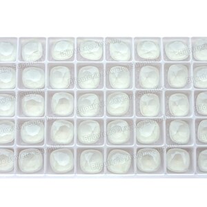May include: A white plastic tray containing 36 clear, square-shaped glass stones. The stones are arranged in a grid pattern.