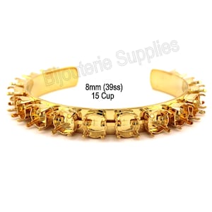 May include: A gold-colored cuff bracelet with a row of square cup settings. The bracelet has the text "8mm (39ss) 15 Cup" printed on it. The bracelet is open at the ends.