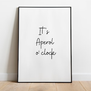 Könnte beinhalten: Ein schwarzer gerahmter Poster mit weißem Hintergrund und dem Text "It's Aperol o'clock" in schwarzer Kursivschrift.