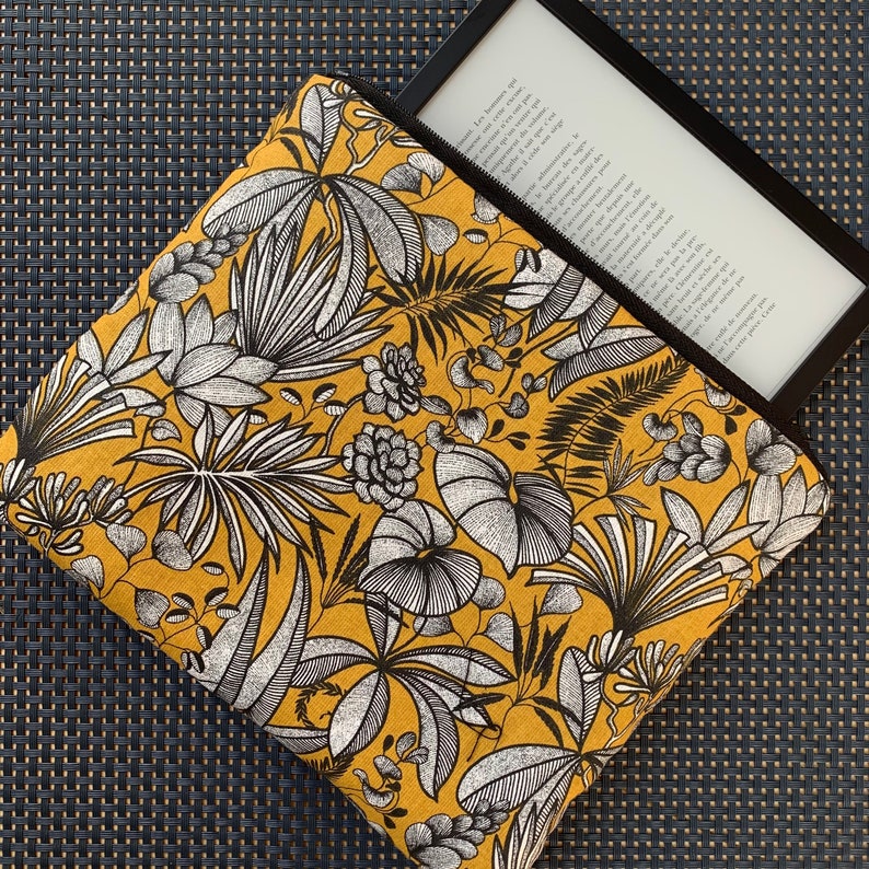 Pu&ograve; includere: Una custodia con cerniera giallo senape con una stampa botanica in bianco e nero, che contiene un e-reader nero. La custodia presenta un motivo dettagliato di foglie e fiori stilizzati. L'e-reader mostra testo sullo schermo.