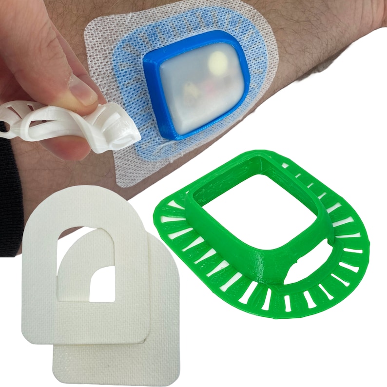 May include: A white medical adhesive bandage with a blue and clear plastic device attached to it. The device has a clear window and a white button. There are two white foam shapes with cutouts and a green plastic ring with a cutout.
