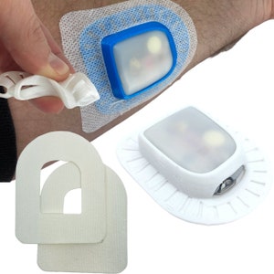 May include: A white medical device with a clear plastic cover and a blue border. The device is attached to a white adhesive bandage. There are two additional white adhesive bandages with a cut-out shape in the center.