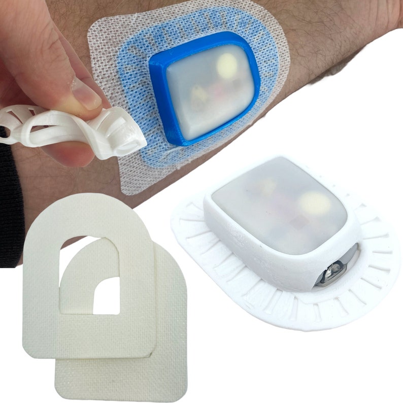 May include: A white medical device with a clear plastic cover and a blue border. The device is attached to a white adhesive bandage. There are two additional white adhesive bandages with a cut-out shape in the center.