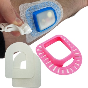 May include: Three 3D printed medical devices. One is a white, semi-circular, adhesive patch with a cut-out in the center. Another is a pink, circular, 3D printed device with a square cut-out in the center. The third is a blue and white device with a clear plastic window.