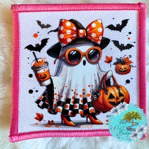May include: A Halloween-themed patch featuring a ghost character wearing sunglasses, a polka-dot bow, and holding a pumpkin-spiced drink and a jack-o'-lantern bag. The ghost is dressed in a black and white checkered skirt and orange heels, with bats and pumpkins in the background.