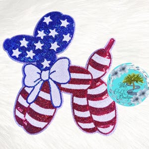 May include: A patriotic balloon dog design in red, white, and blue. The head is blue with white stars, the body is red and white striped, and a white bow is in the center. The design is embellished with sequins.