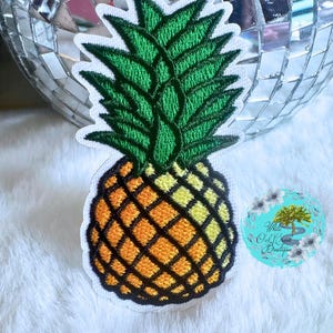 May include: A yellow and orange embroidered pineapple patch with green leaves. The patch is on a white background.