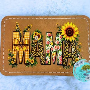 May include: A rectangular patch with the word "MAMA" in a decorative font. The "M" is yellow gingham with a bow, the "A"s are leopard print, and the center "A" is floral. Sunflowers and other flowers surround the letters. The patch is brown with stitched edges.