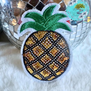 May include: A gold and black sequined pineapple with green felt leaves. The pineapple is a decorative patch.