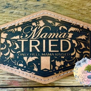 May include: A brown leather patch with the words "Mama Tried" in a decorative font, with the phrase "Only Hell Mama Raised" below. The patch has a dark blue floral design and a stitched border.