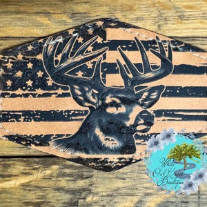 May include: A distressed leather patch with a black and white silhouette of a deer with antlers, superimposed on a black and white American flag design. The text "White Oak Creek Boutique" is visible in the lower right corner.