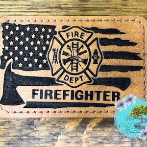 May include: A brown leather patch with a black and white American flag, a firefighter's helmet, an axe, and the words "FIRE DEPT." and "FIREFIGHTER".
