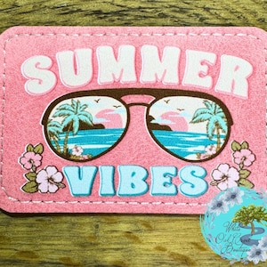May include: Pink felt patch with the text "SUMMER VIBES" in white and blue letters. A pair of sunglasses with a beach scene inside the lenses is above the text.  Pink flowers are on either side of the text.