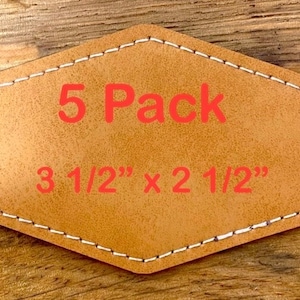 May include: A light brown leather patch with white stitching around the edges. The patch is in a unique shape and has the text "5 Pack" and dimensions of 3 1/2" x 2 1/2" in red. The background is a wooden surface.