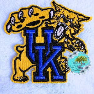 May include: Embroidered patch featuring the letters "UK" in blue, with a yellow wildcat mascot. The patch has a black border and is on a white background. The wildcat is snarling and has its claws out.