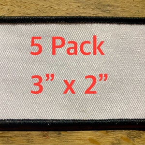 May include: Five white iron-on patches with black stitching around the edges. The patches are 3 inches by 2 inches and say "5 Pack" and "3" x 2" in red.